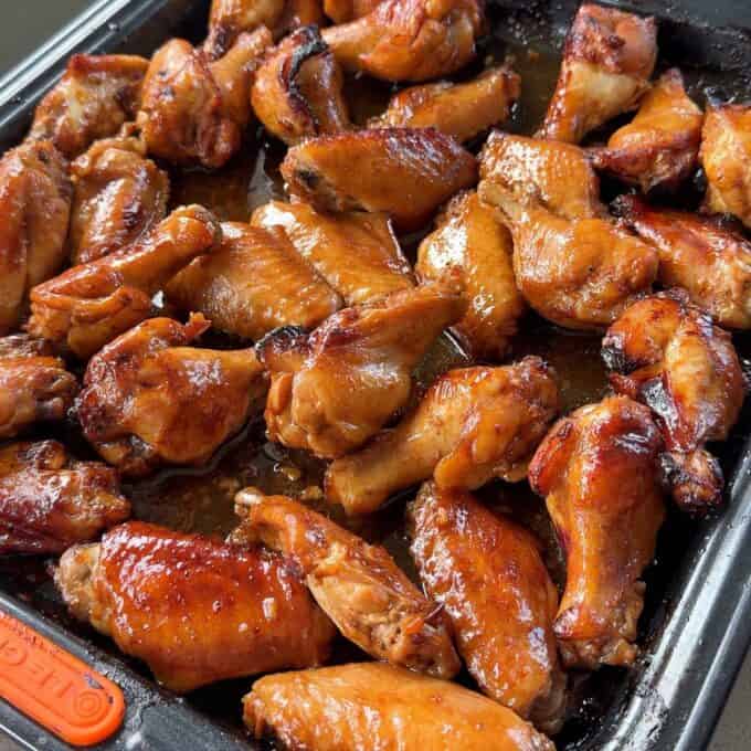 Honey Chicken Nibbles A tray filled with glazed, baked chicken wings arranged closely together, showing a shiny, caramelized surface.