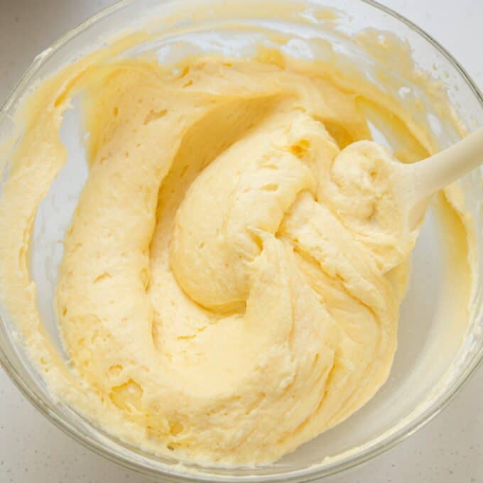 Limoncello Tiramisu Glass bowl filled with thick, creamy yellow cake batter being stirred with a white spatula.