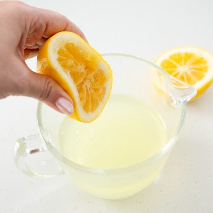 Limoncello Tiramisu A hand squeezing half a lemon over a glass measuring cup filled with lemon juice, with another lemon half on the counter.