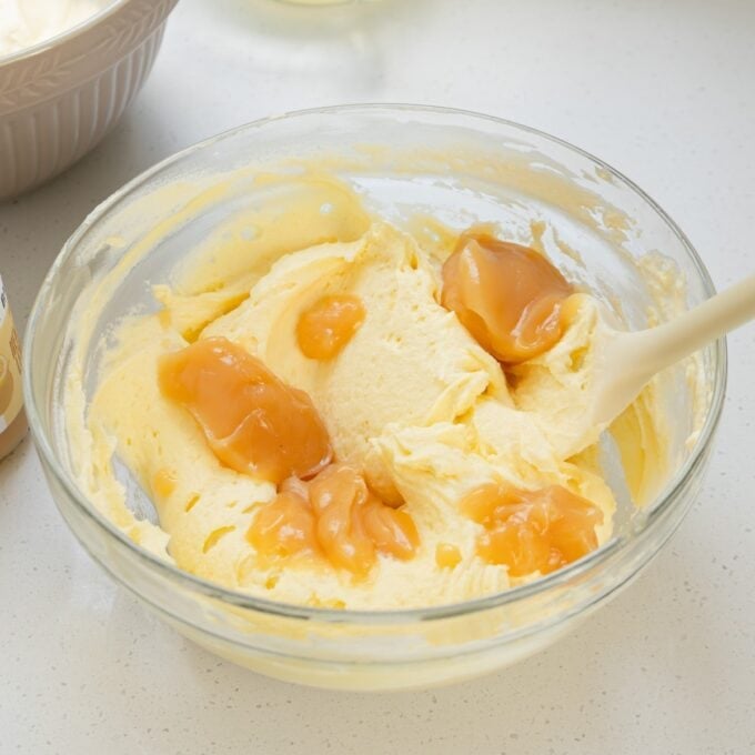 Limoncello Tiramisu A glass bowl containing yellow cake batter with several dollops of caramel sauce on top, and a white spatula resting in the mixture.