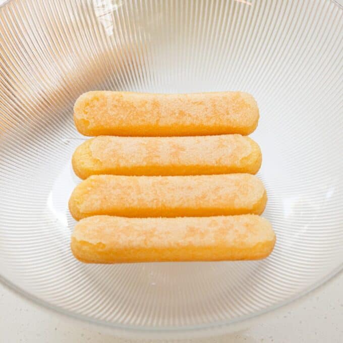 Limoncello Tiramisu Four sugar-coated ladyfinger biscuits are arranged in a single layer inside a large, clear ribbed glass bowl.
