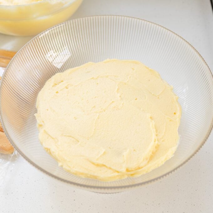 Limoncello Tiramisu A glass bowl filled with a smooth, yellow, creamy mixture sits on a white countertop.