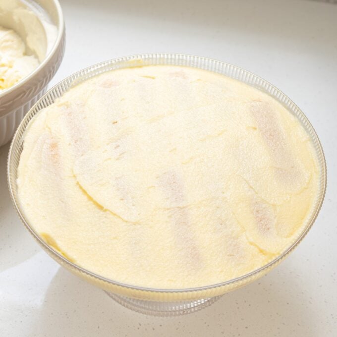 Limoncello Tiramisu A glass bowl filled with a layer of creamy, pale yellow tiramisu, with faint lines of ladyfingers visible beneath the surface.