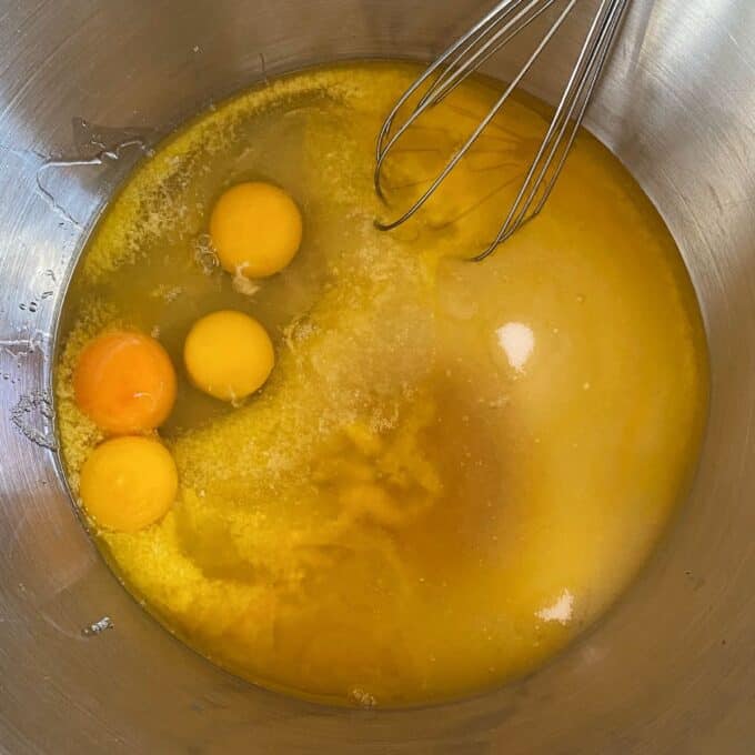 Big One Bowl Chocolate Brownie Four raw eggs, sugar, and melted butter in a metal mixing bowl with a whisk.