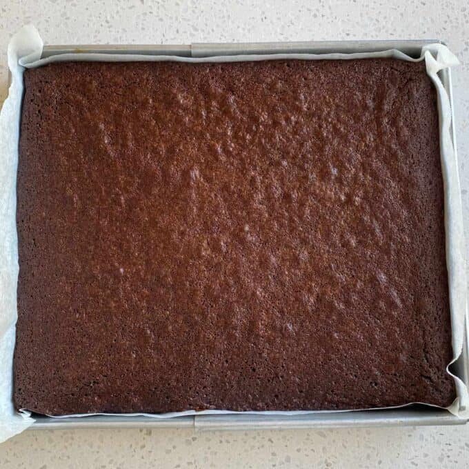 Big One Bowl Chocolate Brownie A rectangular tray of baked chocolate brownies sits on a parchment-lined baking dish on a light-colored countertop.