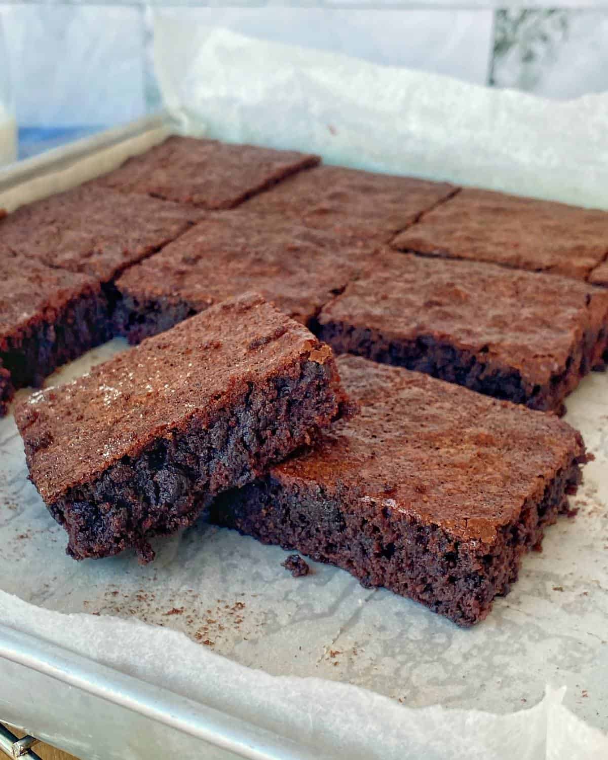 Big One Bowl Chocolate Brownie A tray of chocolate brownies, cut into square pieces, with one brownie slightly propped up to show its texture.