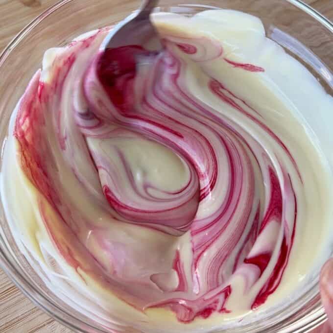 Speckled Mini Egg Slice A spoon stirs red food coloring into white yogurt or cream in a glass bowl, creating a marbled pattern.