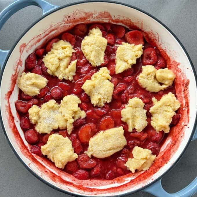 Strawberry Cobbler A round baking dish filled with cherry filling and topped with uneven dollops of biscuit dough, ready to be baked.