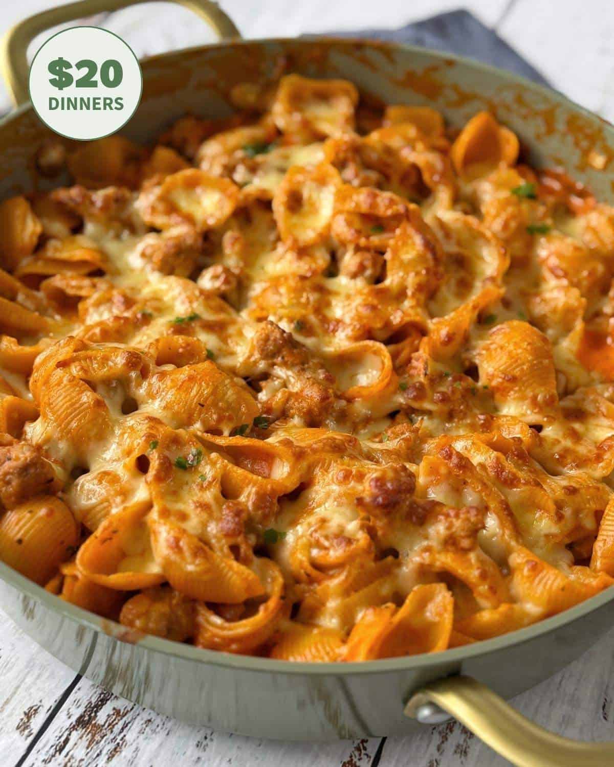 Large skillet filled with cheesy pasta shells and ground meat in tomato sauce. A green badge in the corner reads $20 dinners.