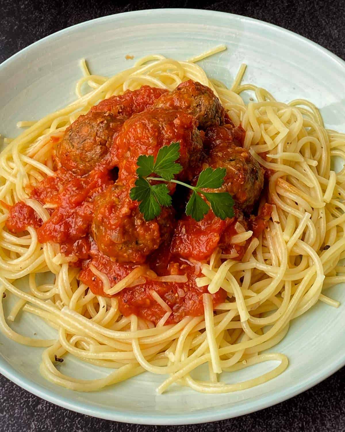 Veggie-Packed Meatballs A plate of spaghetti topped with tomato sauce, meatballs, and garnished with a sprig of parsley.