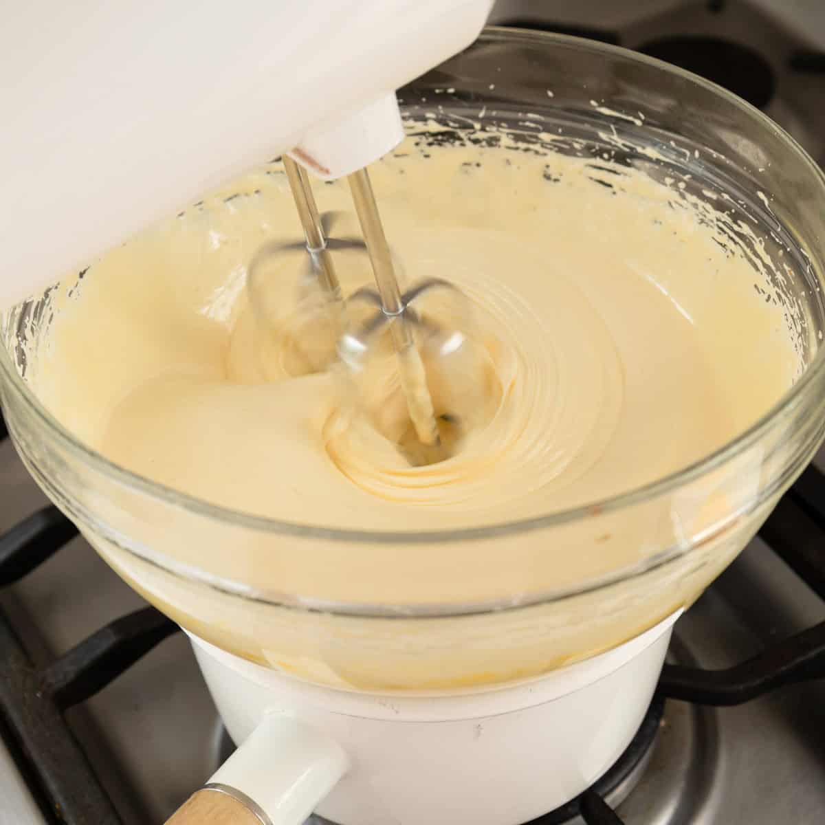 Berry Semifreddo A hand mixer blends a creamy batter in a glass bowl set over a saucepan on a stove, likely for a double boiler method.