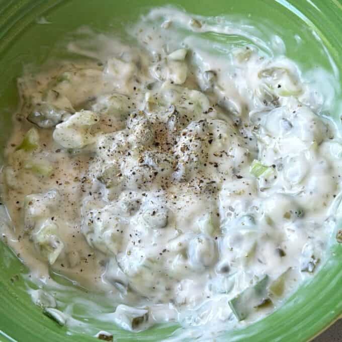 Crispy Panko Fish Bites A green bowl filled with creamy dip or sauce containing chopped pickles and topped with a sprinkle of ground black pepper.