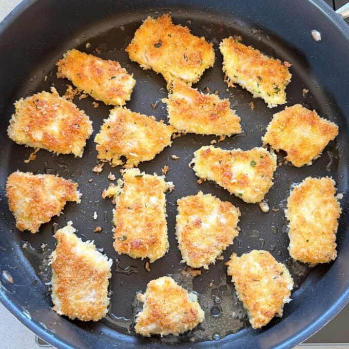 Crispy Panko Fish Bites Breaded and pan-fried chicken pieces are arranged in a single layer in a black nonstick skillet.