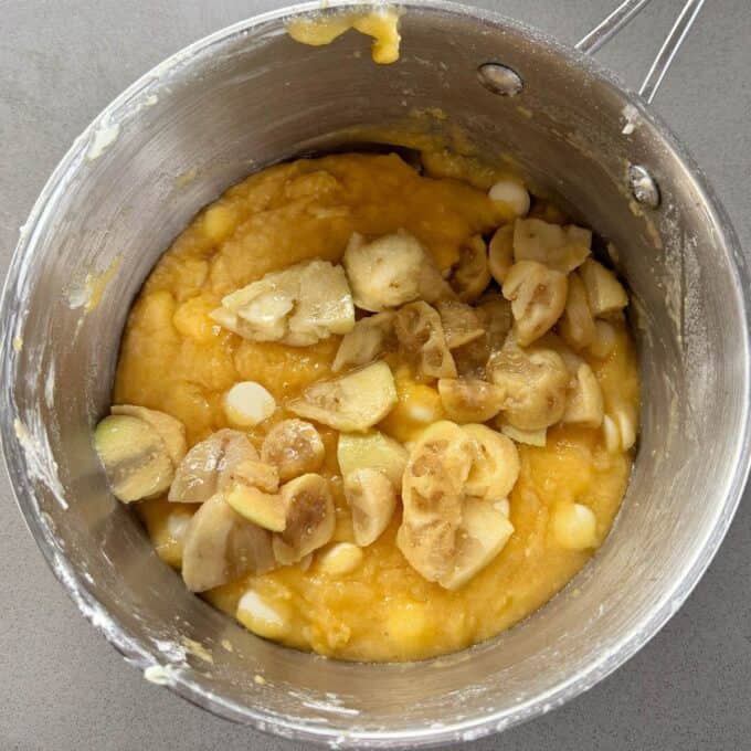 Feijoa and White Blondie A metal pot containing a thick yellow batter mixed with feijoa slices and white chocolate chips on a gray countertop.