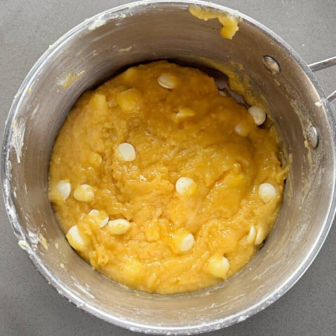 Feijoa and White Blondie A metal mixing bowl containing thick yellow batter with white chocolate chips mixed in, viewed from above on a gray surface.