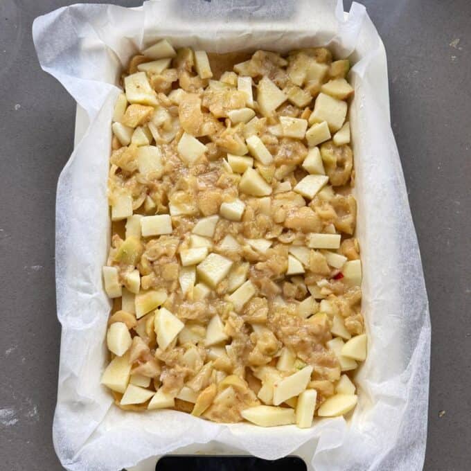 Feijoa and Apple Crumble Slice A baking dish lined with parchment paper contains an unbaked mixture of chopped apples and dough, ready to be baked.