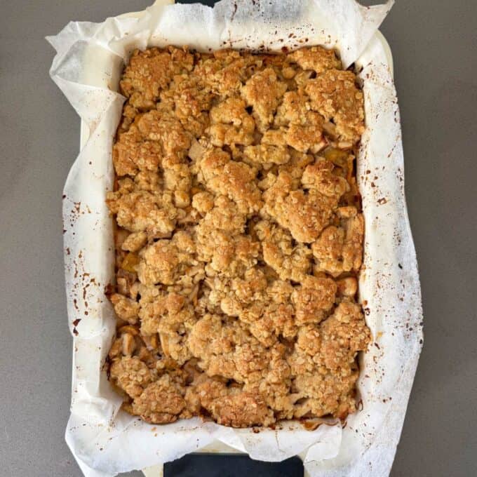 Feijoa and Apple Crumble Slice A baked oat and fruit crumble sits in a parchment-lined rectangular dish on a gray surface.