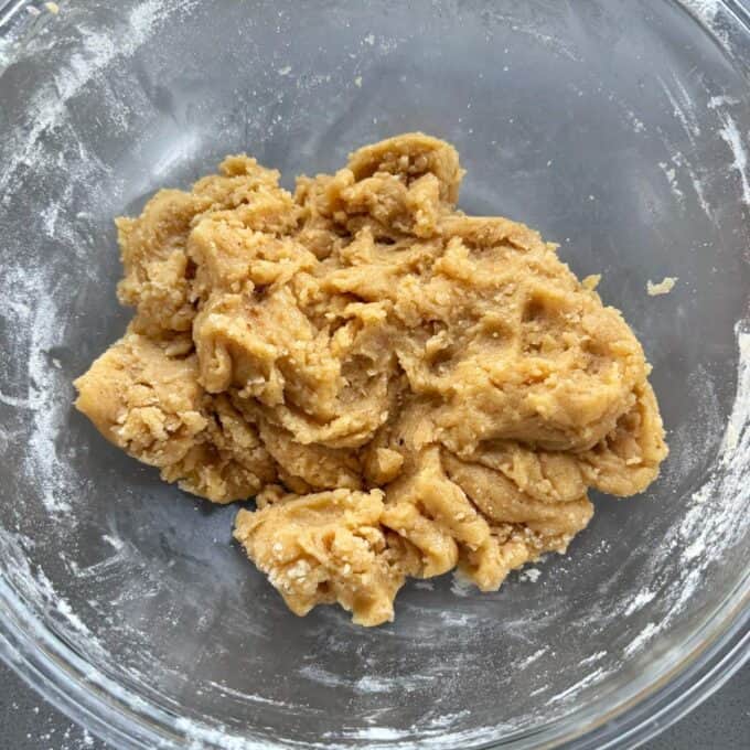 Feijoa and Apple Crumble Slice A clear glass bowl containing a lump of raw cookie dough on a gray surface.