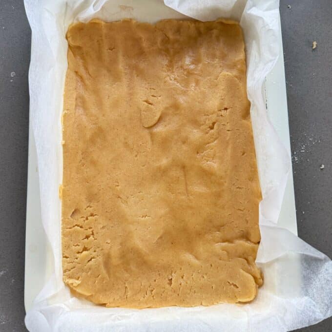 Feijoa and Apple Crumble Slice A rectangular pan lined with parchment paper contains an even layer of unbaked dough pressed flat.