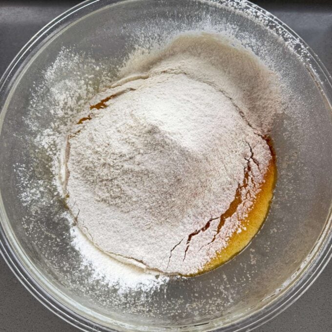 Feijoa and Apple Crumble Slice A glass bowl containing a mound of flour on top of a yellowish liquid mixture, ready to be mixed together.