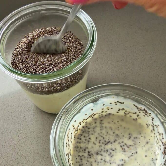 Feijoa Chia Puddings Two glass jars with yogurt and chia seeds; one jar is being stirred with a spoon while the other shows the mixture after the seeds have absorbed liquid.