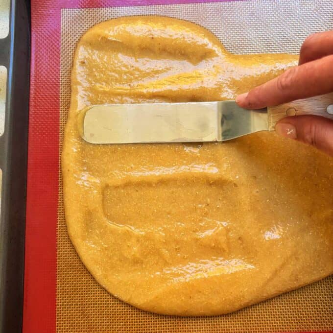 Feijoa Leather A hand uses an offset spatula to spread a light brown batter evenly on a silicone baking mat.