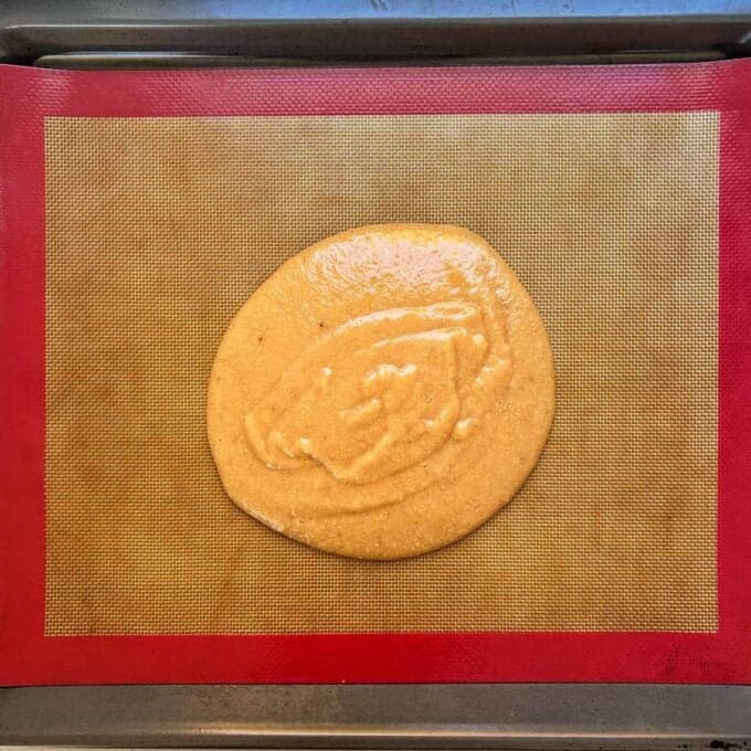 Feijoa Leather A round pool of thick batter spread on a silicone baking mat placed on a metal baking sheet.