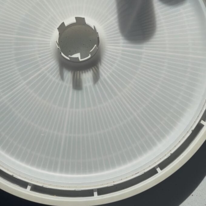 Feijoa Leather A close-up of a white circular plastic tray with a vented design and central opening, partially in shadow.
