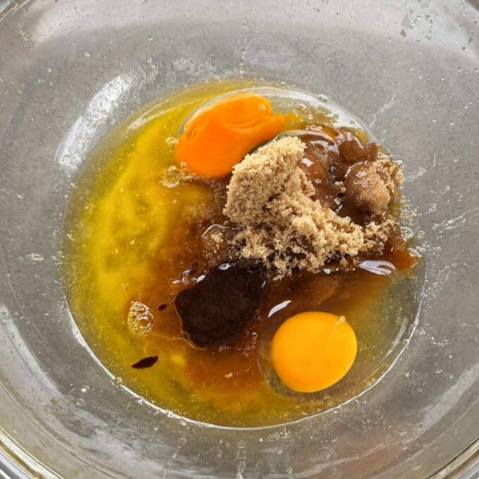 Feijoa Loaf A clear glass bowl containing two raw eggs, melted butter, brown sugar, and vanilla extract, ready to be mixed.