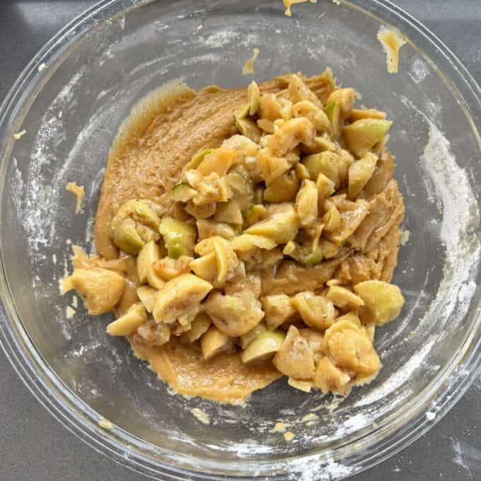 Feijoa Loaf A glass bowl containing cookie dough mixed with chopped green apples, placed on a gray surface.