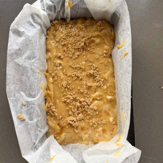 Feijoa Loaf Unbaked banana bread batter in a parchment-lined loaf pan, topped with a sprinkle of brown sugar, on a gray countertop.