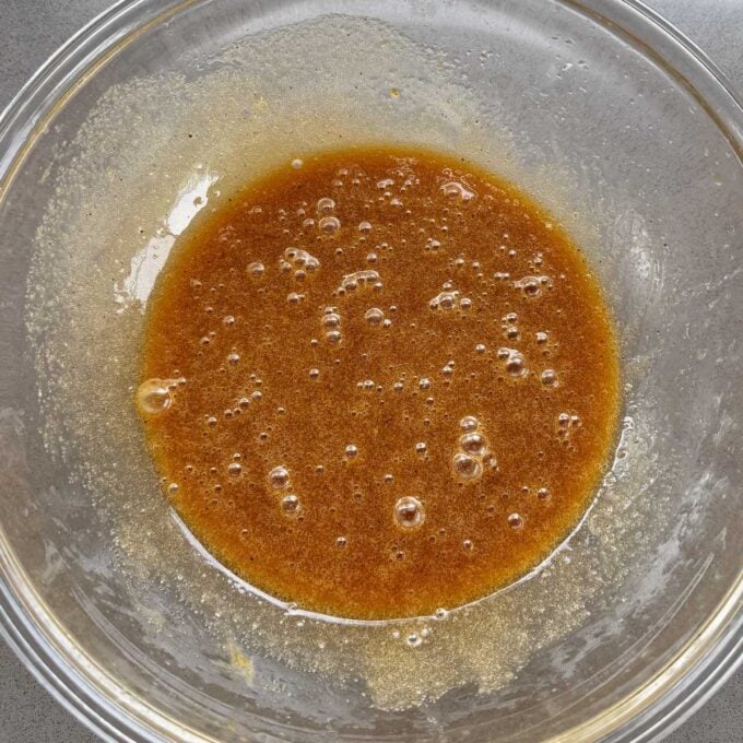 Feijoa Loaf A glass bowl containing a light brown, bubbly liquid mixture on a gray surface.