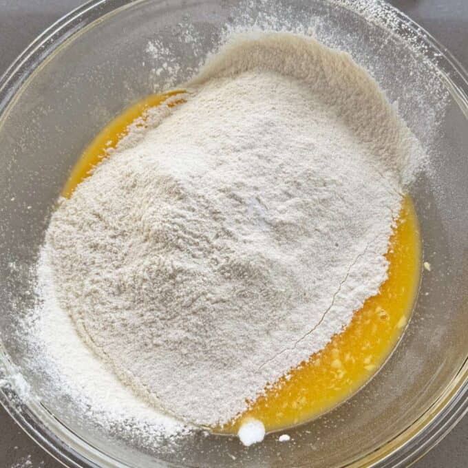 Feijoa Muffins A glass bowl containing a mound of flour on top of a yellow liquid mixture, ready to be mixed together.