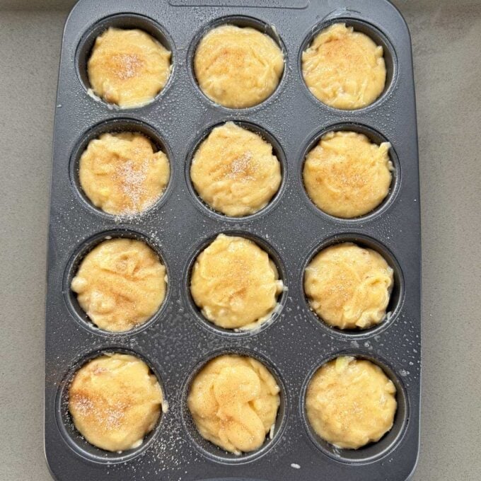 Feijoa Muffins A muffin tin filled with twelve portions of unbaked batter, some topped with a sprinkle of sugar, sits on a countertop.