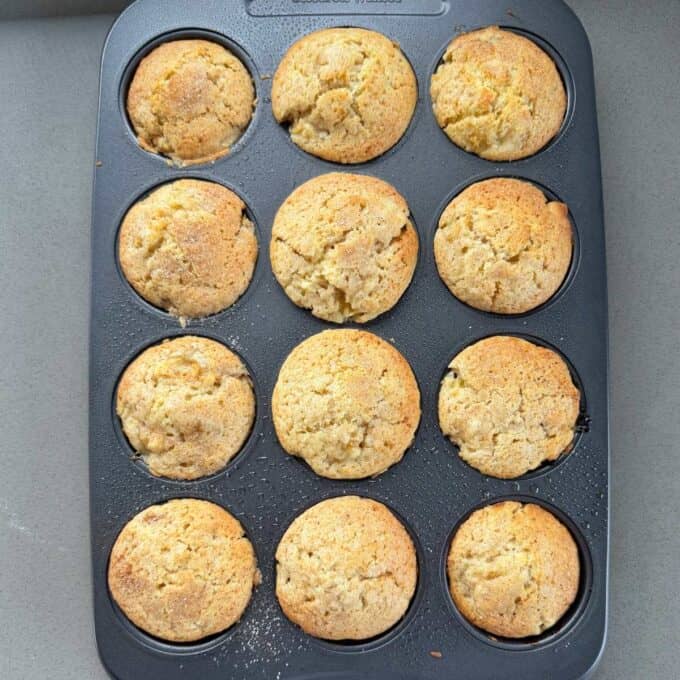 Feijoa Muffins A muffin tin filled with twelve freshly baked, golden-brown muffins on a gray countertop.
