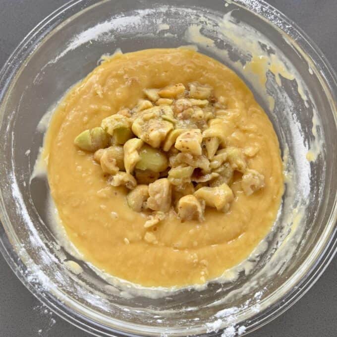 Feijoa Muffins A glass bowl containing thick yellow batter with chopped apples and nuts in the center, ready to be mixed.