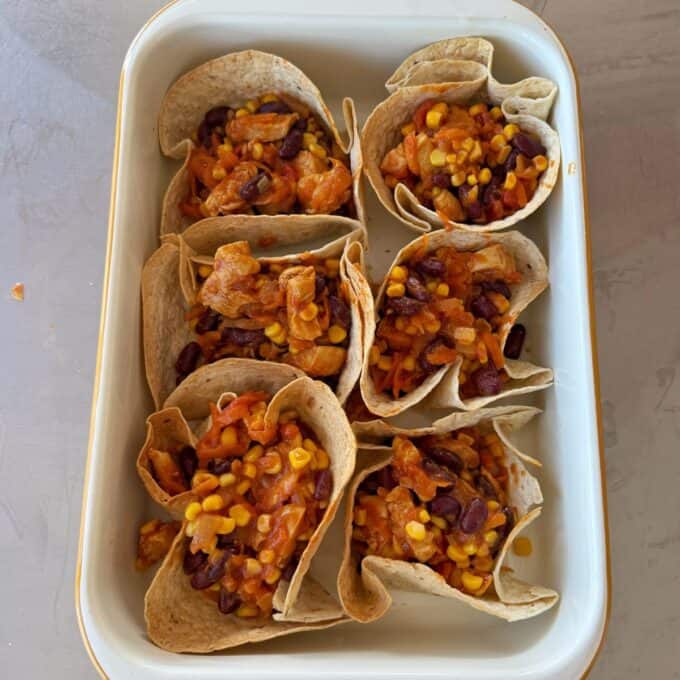 Loaded Chicken Tortilla Cups Six tortilla cups filled with a mixture of beans, corn, and diced vegetables sit in a white baking dish.