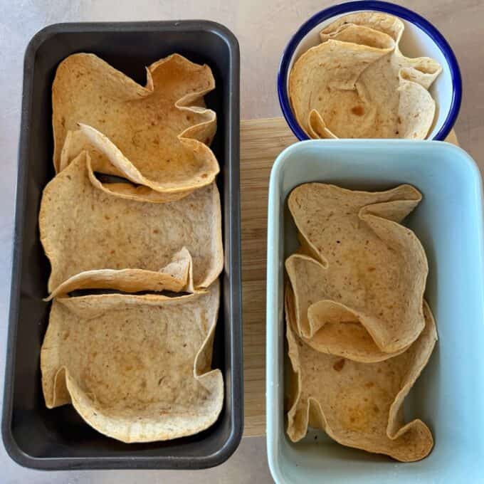 Loaded Chicken Tortilla Cups Four tortilla wraps are shaped into bowls using two loaf pans and one round bowl on a countertop.