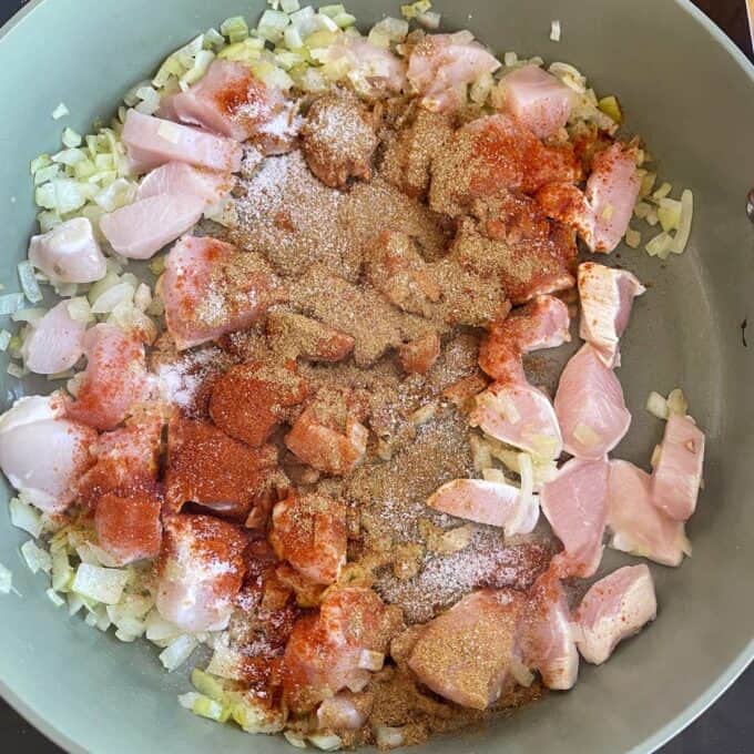 Loaded Chicken Tortilla Cups Chopped raw chicken, onions, and assorted ground spices cooking in a pan.