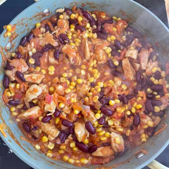 Loaded Chicken Tortilla Cups A pan filled with a cooked mixture of diced meat, kidney beans, corn, tomatoes, and sauce.