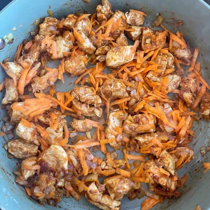Loaded Chicken Tortilla Cups Chopped chicken and shredded carrots being sautéed with onions and spices in a frying pan.