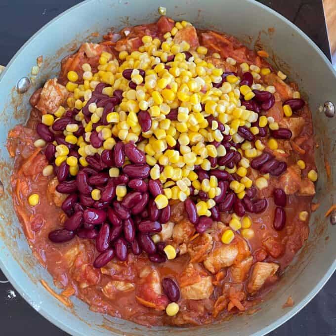 Loaded Chicken Tortilla Cups A pan filled with a tomato-based stew containing chunks of meat, topped with kidney beans and corn kernels.