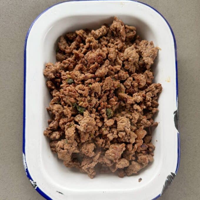 One Pot Beef Mince Noodles A white and blue rectangular dish filled with cooked ground beef, placed on a gray surface.