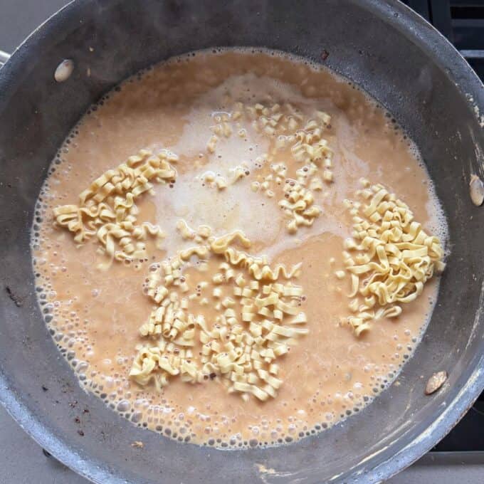 One Pot Beef Mince Noodles Uncooked instant ramen noodles in a pan with boiling broth or soup, beginning to soften and separate.