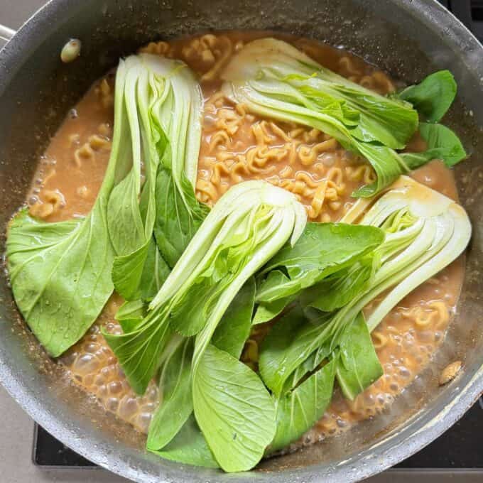 One Pot Beef Mince Noodles A pot of ramen noodles cooking in broth topped with fresh bok choy.