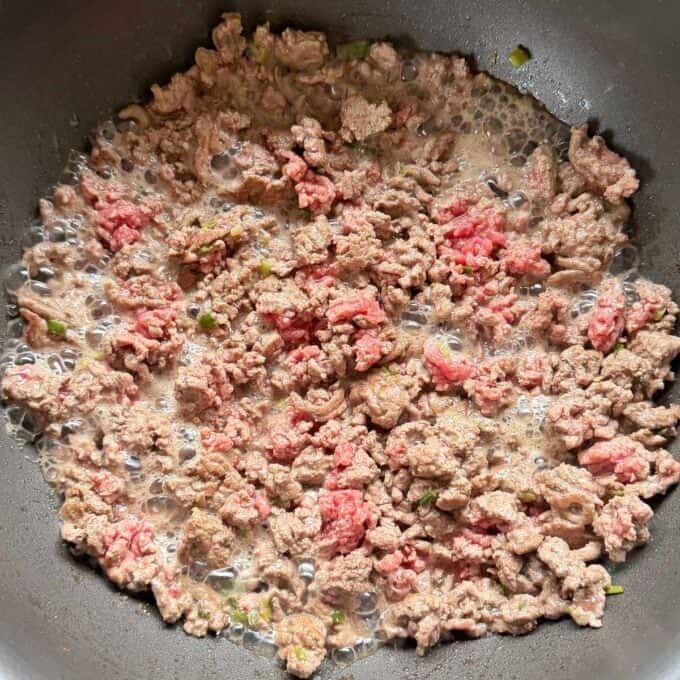 One Pot Beef Mince Noodles Ground beef and chopped green peppers being browned in a skillet, with some pieces still partially pink and others cooked through.