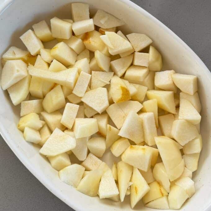 Feijoa and Pear Crumble A white oval dish filled with evenly chopped pieces of peeled apple on a gray surface.
