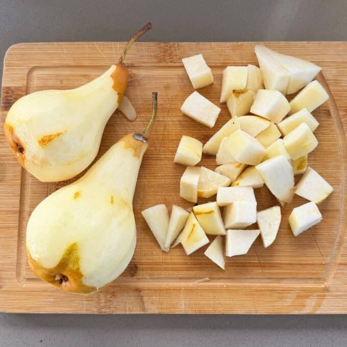 Feijoa and Pear Crumble Two peeled pears and a pile of diced pear pieces are arranged on a wooden cutting board.
