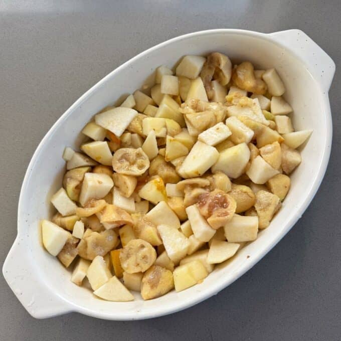 Feijoa and Pear Crumble A white oval dish filled with chopped apples and bananas on a gray countertop.