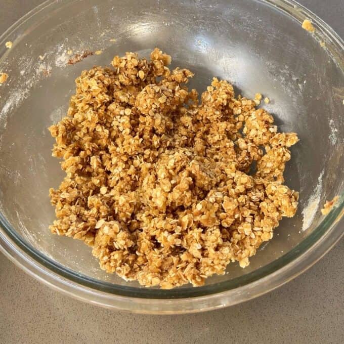 Feijoa and Pear Crumble A glass bowl contains a mixture of oats, brown sugar, and other baking ingredients, partially mixed and ready for baking.